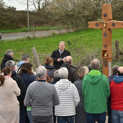 Viele Menschen stehen vor einem Wegekreuz.