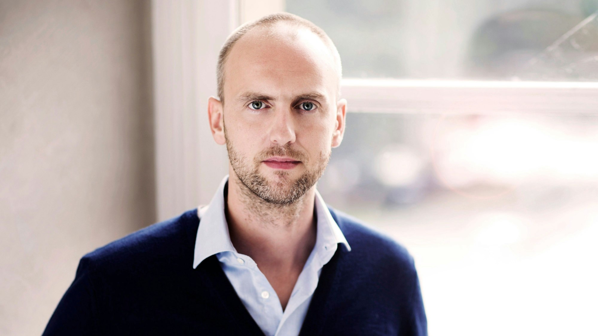 Peter Dijkstra steht mit offenem Hemdkragen vor einem Fenster.