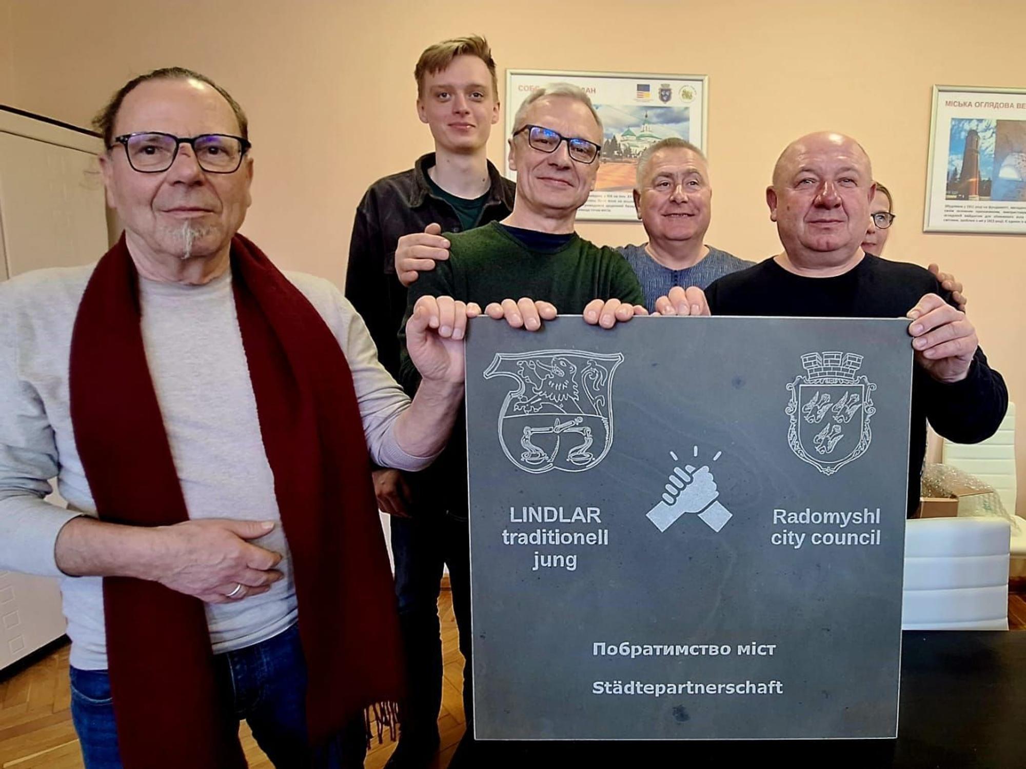 Das Foto zeigt Gäste und Gastgeber mit einer Grauwacketafel und einer zweisprachigen Aufschrift zur Städtepartnerschaft.