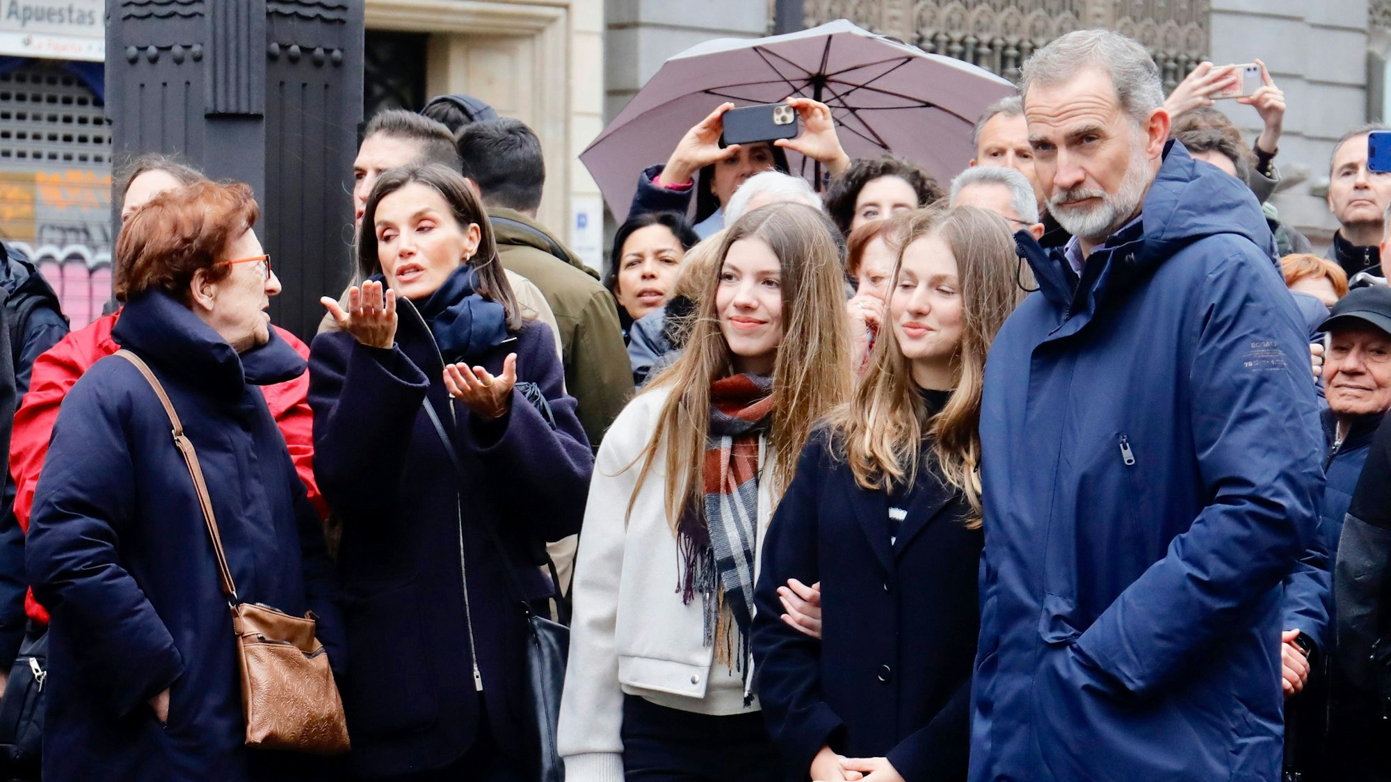 Königin Letizia unterhält sich mit einer Frau, Während Sofia und Leonor mit ihrem Vater Felipe die Osterprozession bestaunen.