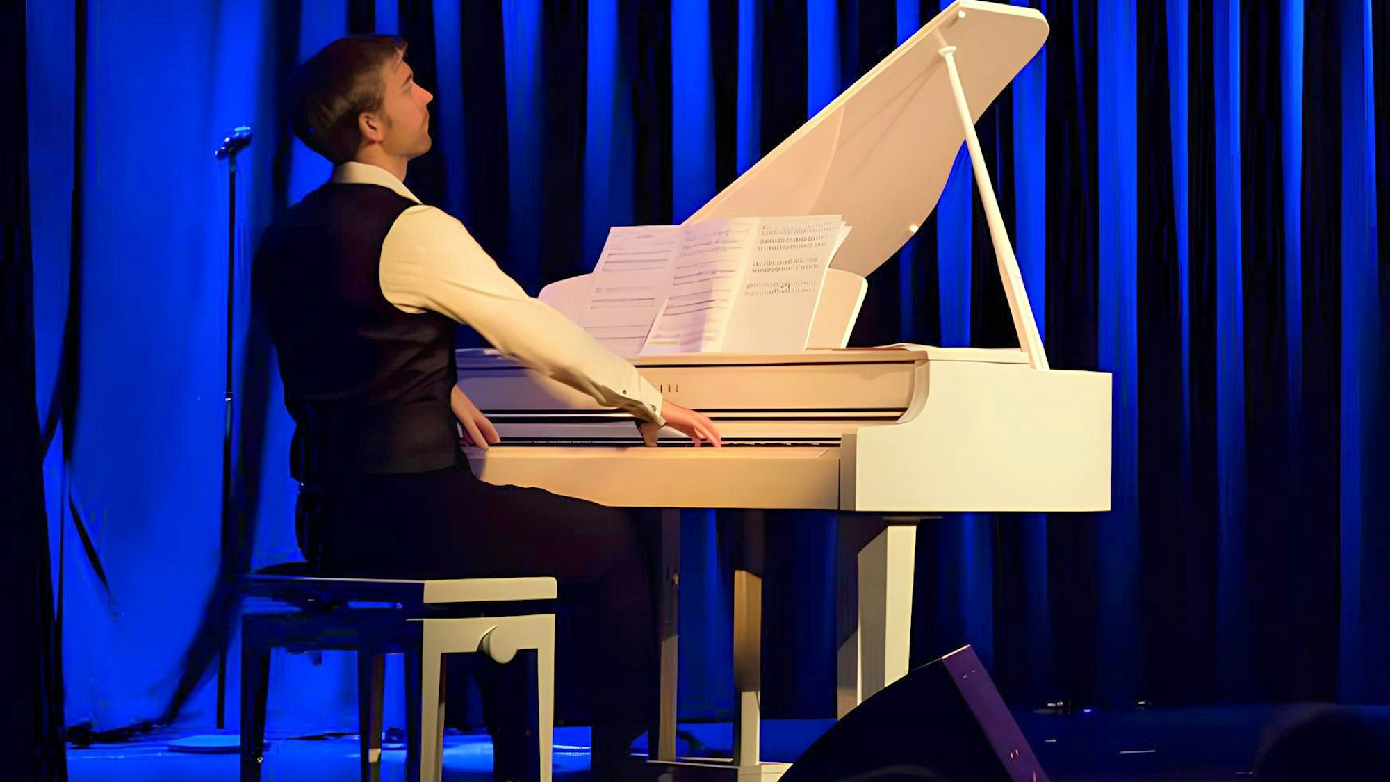 Der Musiker sitzt an einem weißen Flügel, er spielt, wirkt in sich versunken.
