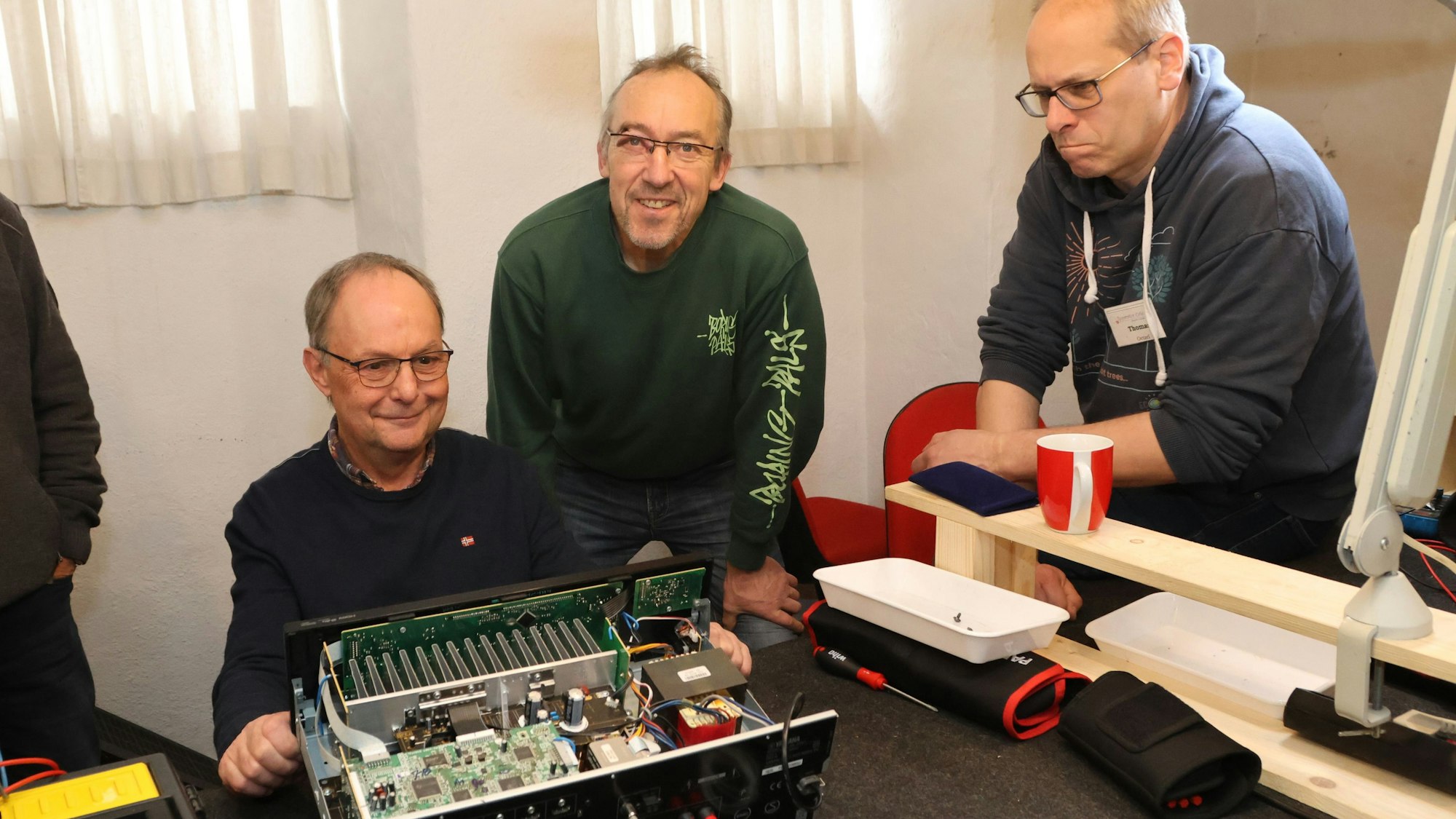 Der Ehrenamtler Diethelm Noll (links), repariert den Verstärker des Waldbrölers Martin Klein (Mitte) im Waldbröler Repair-Café, ein weiterer Helfer gibt Tipps von der Seite.