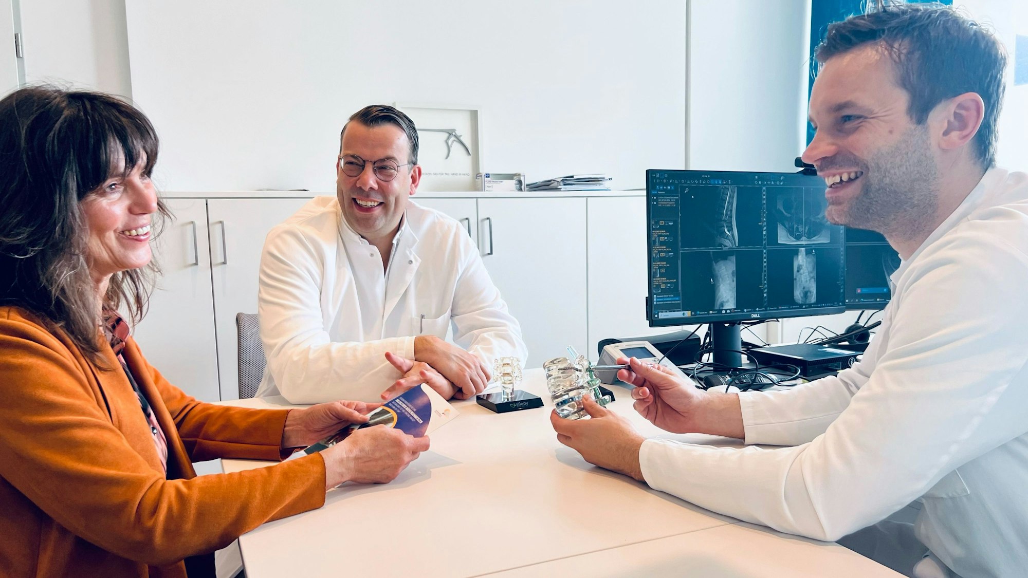 Birgit Sauer (l.) sitzt an einem Tisch mit den Ärzten Jan Bredow (r.) und Paul Martin Bansmann (M.) am Krankenhaus Porz.