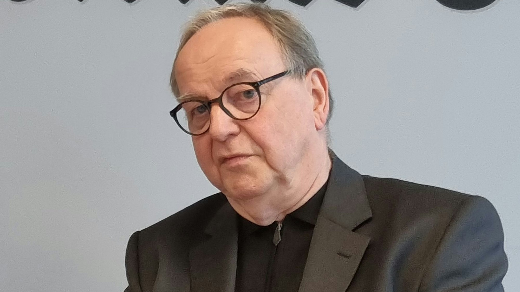 Das Bild zeigt einen sitzenden Mann vor einer Wand.