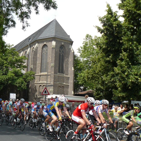Rennradfahrer fahren im Pulk, im Hintergrund ist eine Kirche zu sehen.