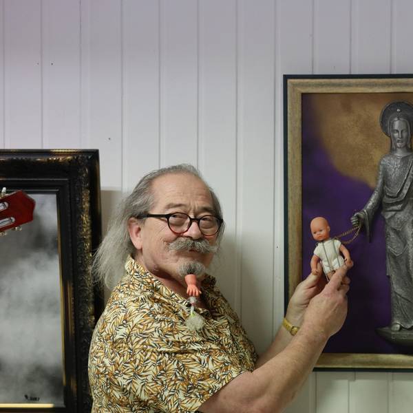 Uwe Rhiem hält eine Puppe vor ein Bild mit einer Christusfigur.