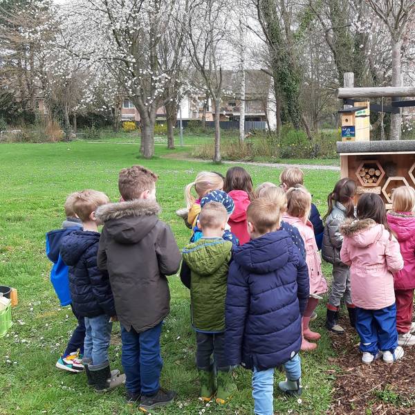 Eine Gruppe von Kindern steht vor dem hölzernen Insektenhotel in der Grünanlage vor der Kita.