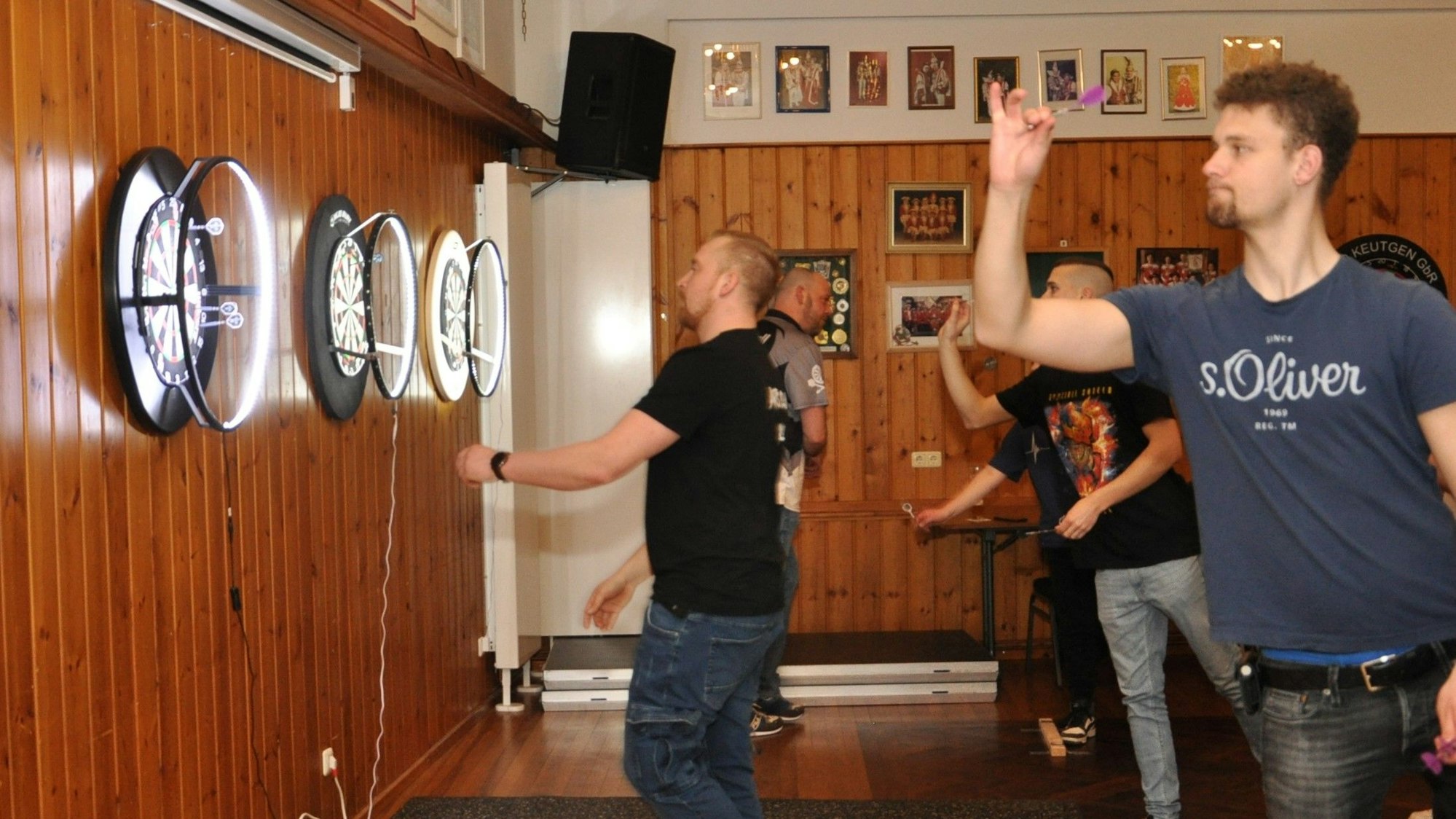 Darts-Spieler werfen ihre Pfeile auf Scheiben, die an der mit Holz verkleideten Wand hängen.