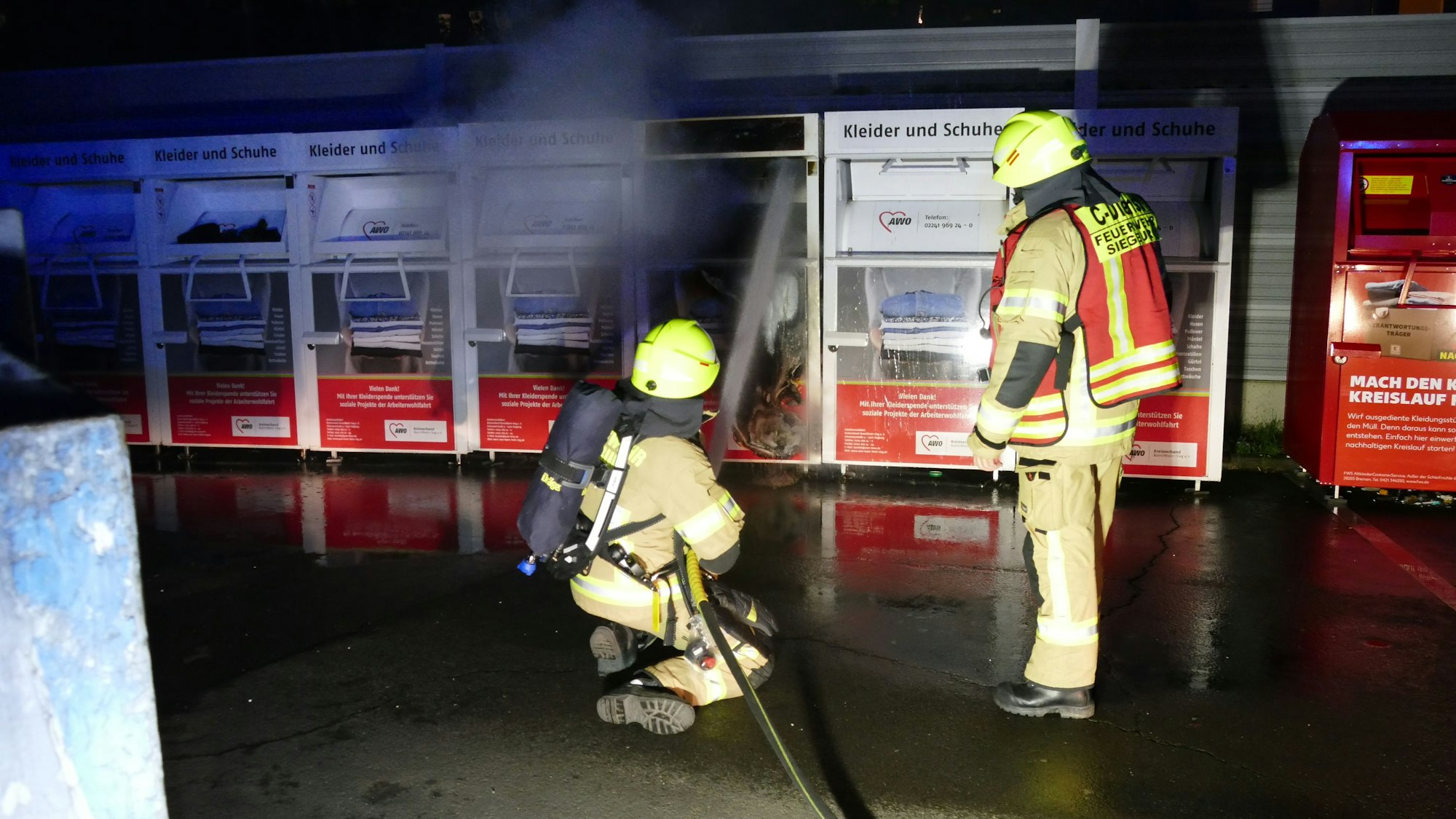 Ein brennender Altkleidercontainer in einer Reihe gleicher Container.