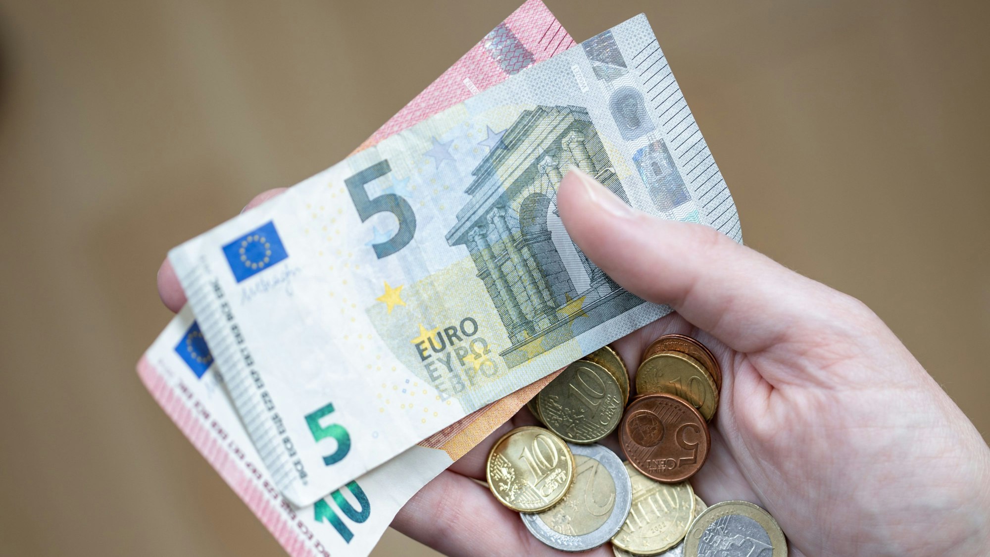 Eine Frau hält Geldscheine und Münzen in der Hand.