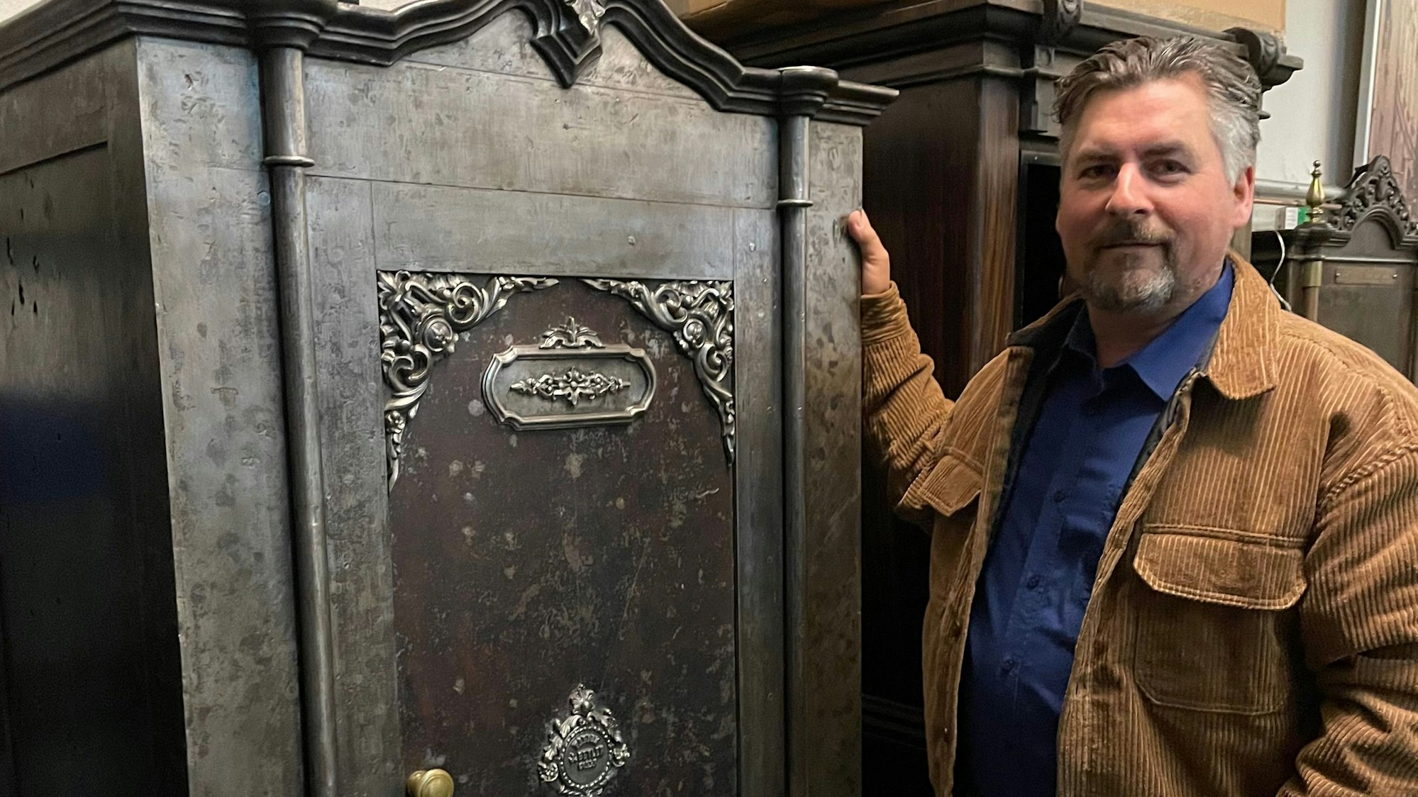 Lars Jelonnek steht neben einem Tresor um 1900 der Firma Beylen, der einen drei stufigen Schließungsmechanismus hat.
