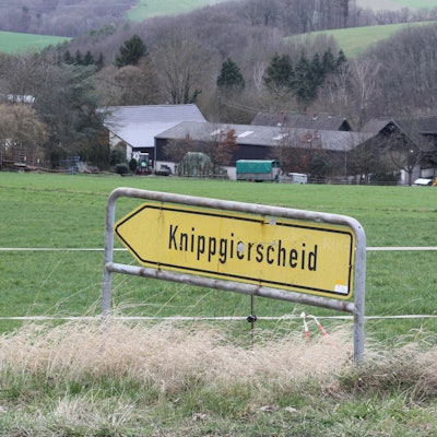 Blick über ein landwirtschaftliche Wiese auf ein Gehöft mit einem Schild im Vordergrund, das den Weg zum Dorf Knippgierscheid zeigt.