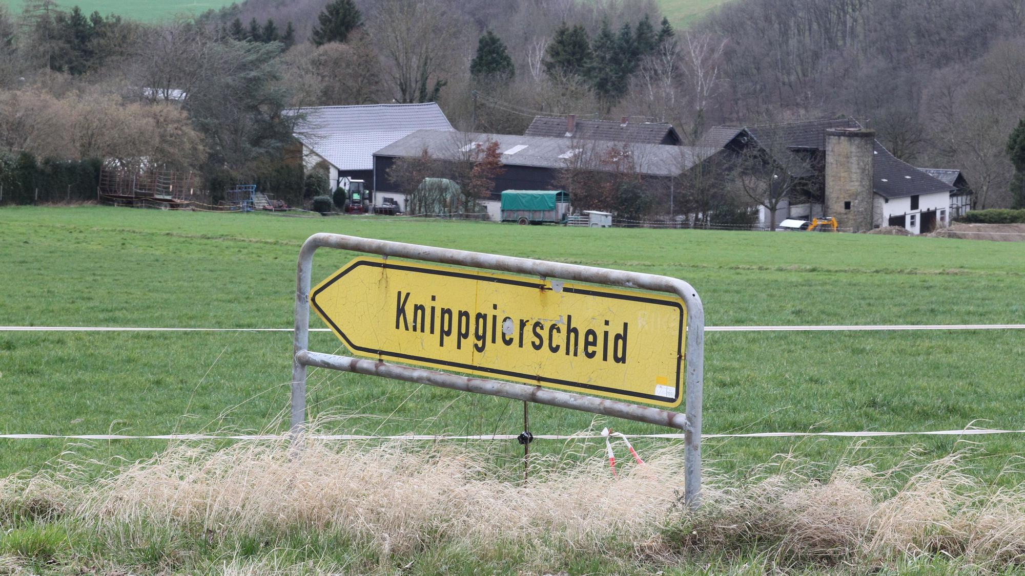 Blick über ein landwirtschaftliche Wiese auf ein Gehöft mit einem Schild im Vordergrund, das den Weg zum Dorf Knippgierscheid zeigt.