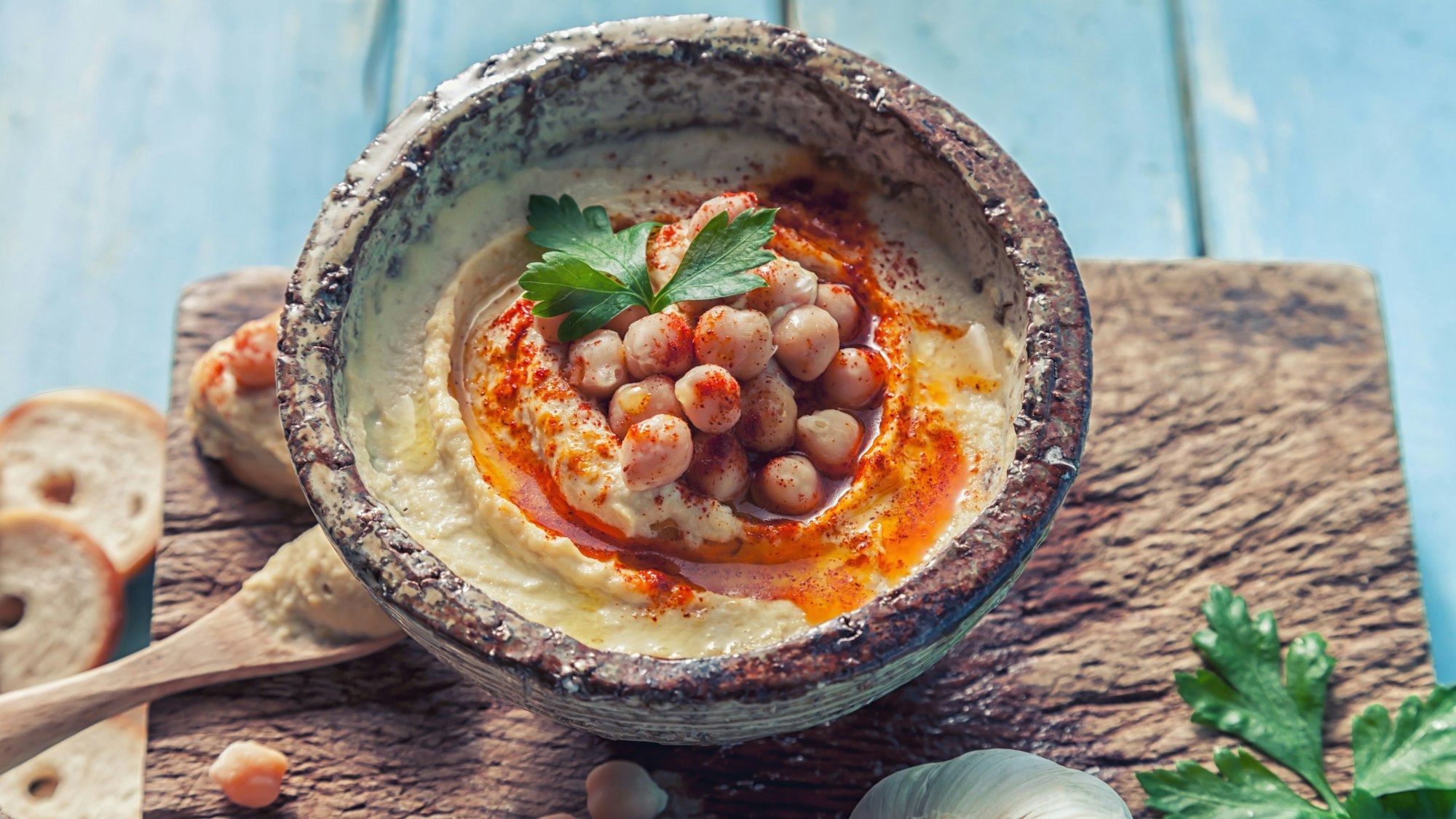 Schale mit Hummus, dekoriert mit Kichererbsen, Petersilie und Paprikapulver