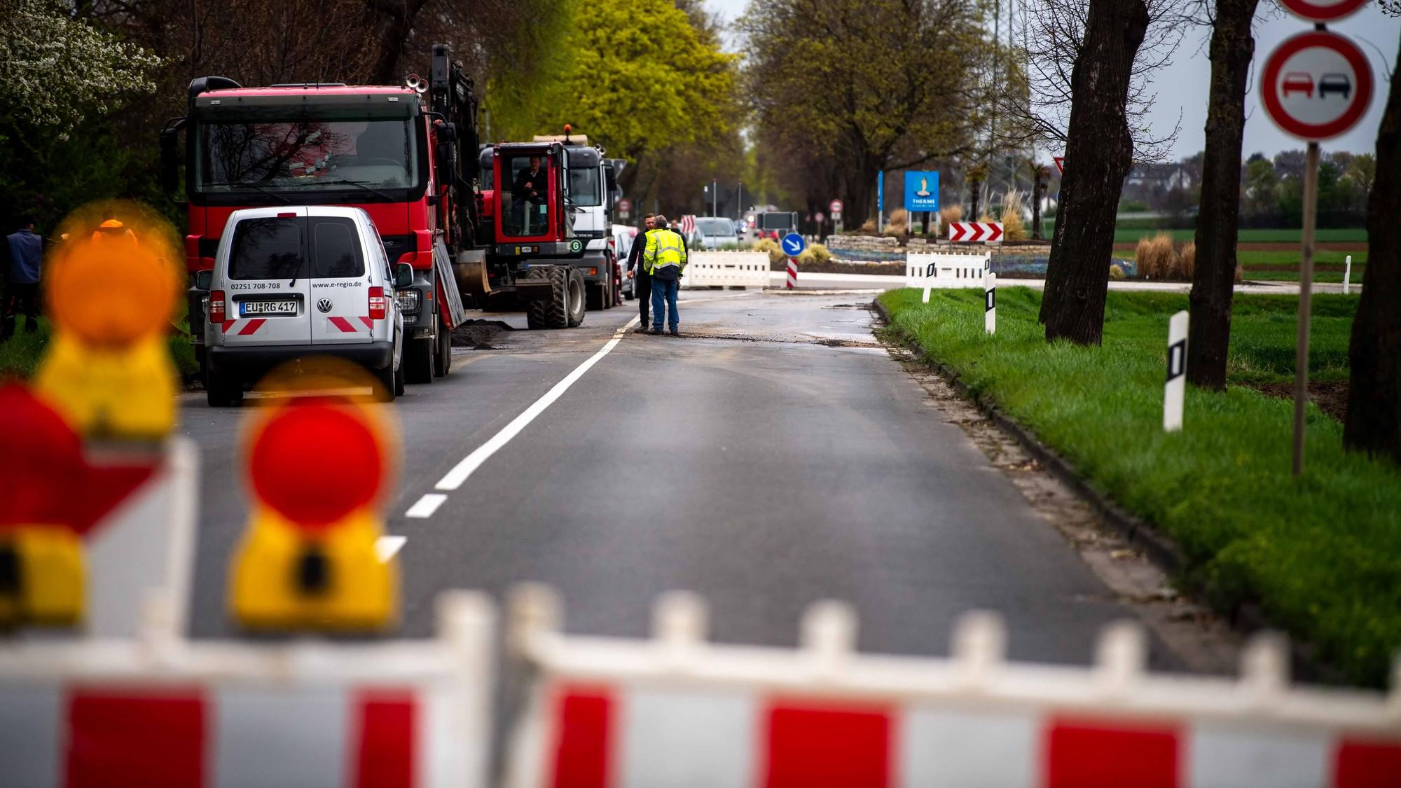 Auf einer Straße in Euskirchen stehen Absperrbaken, dahinter sind Baustellenfahrzeuge zu sehen.