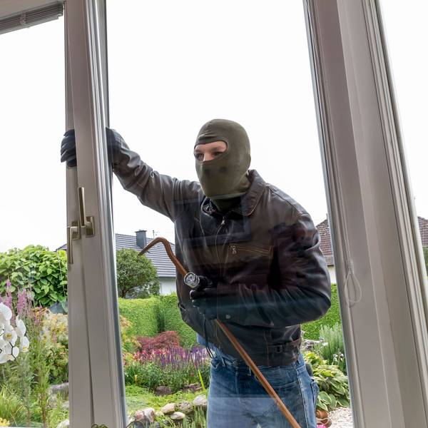 Ein Einbrecher macht sich an einem Fenster zu schaffen.