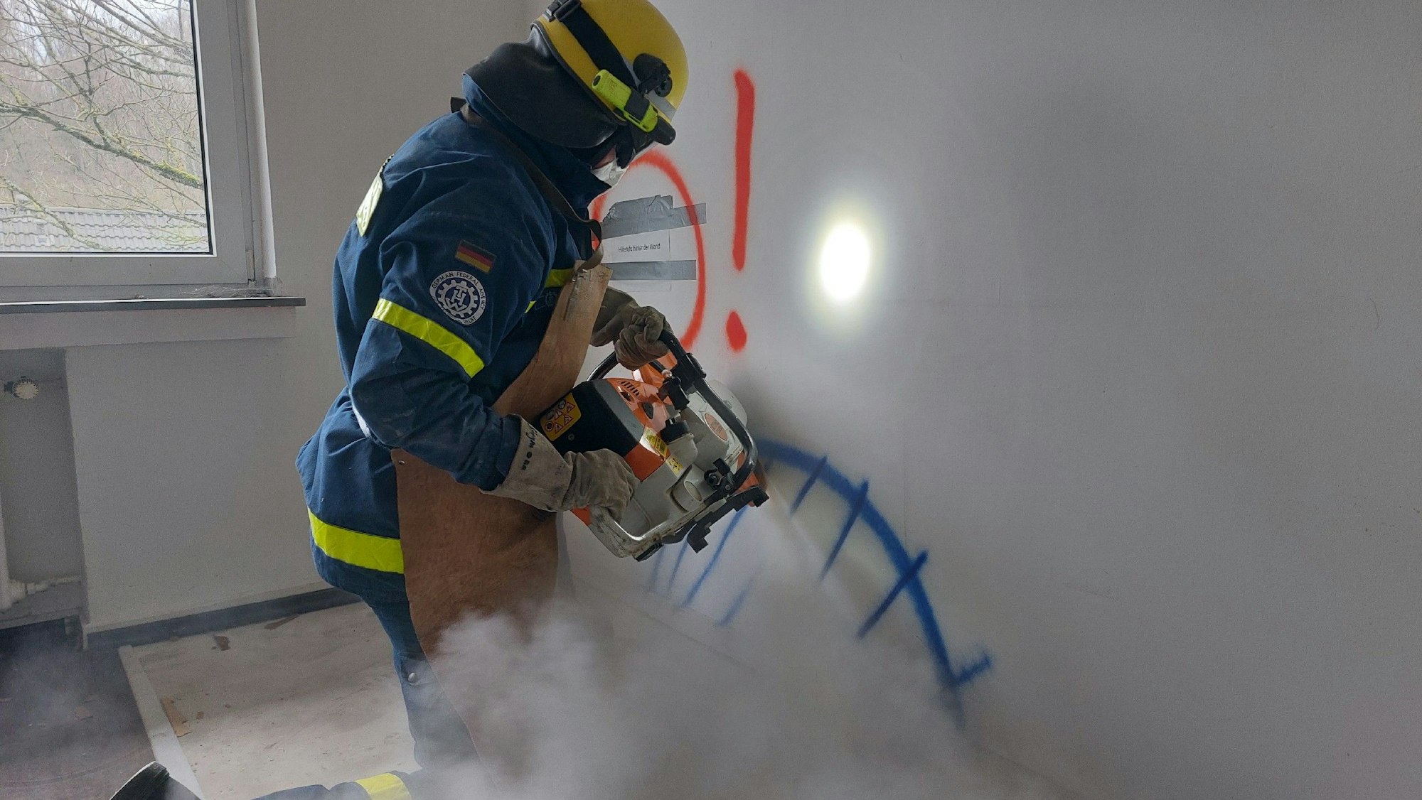 Ein THW-Helfer schneidet mit schwerem Gerät ein Loch in eine Wand.