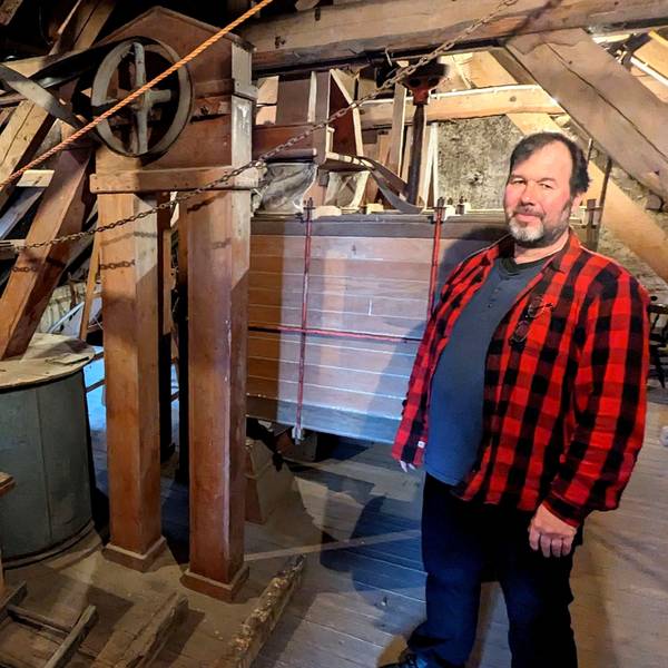 Wolfgang Pütz zeigt die alten Gerätschaften im Dachboden der Hauserbachmühle. Er trägt ein rot-kariertes Holzfällerhemd.
