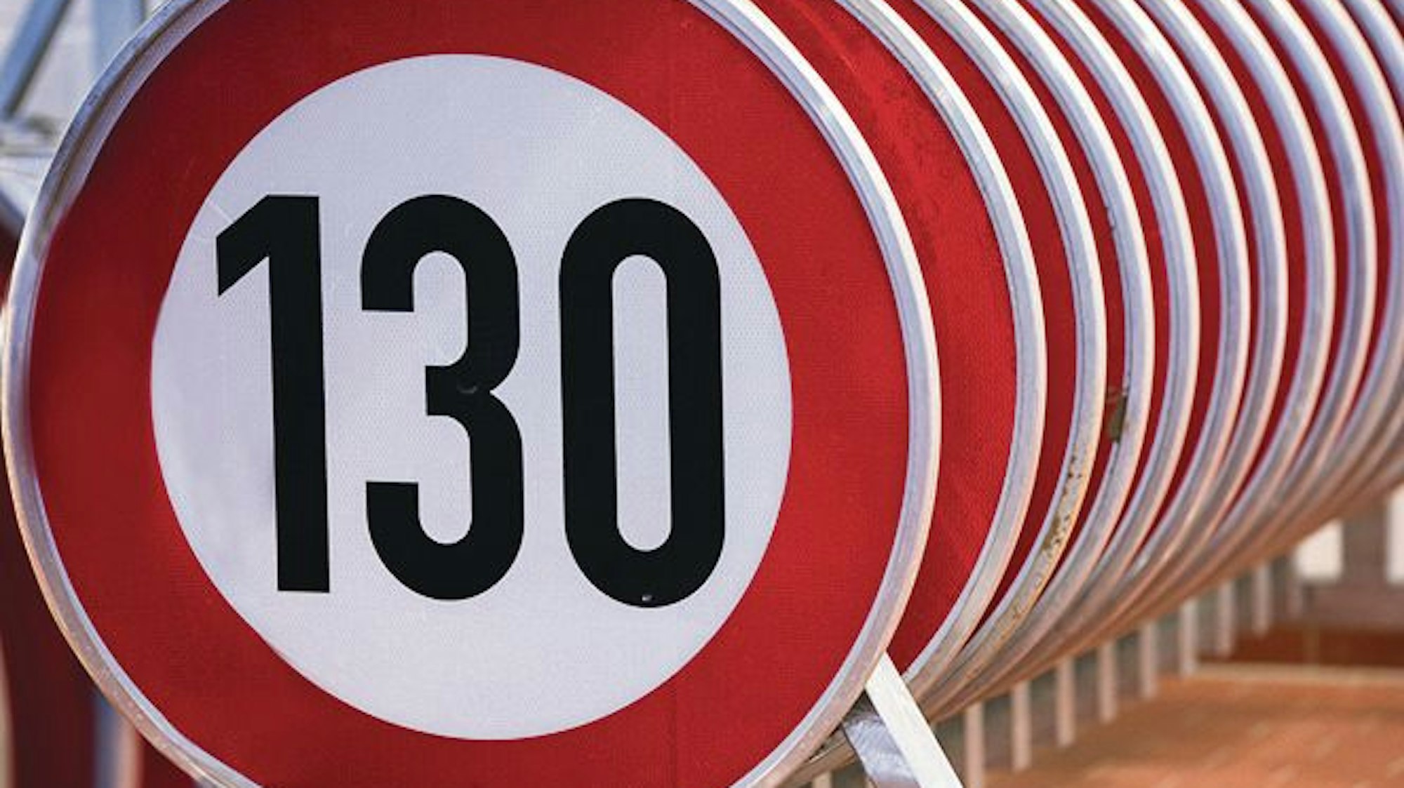 Hintereinander aufgereiht stehen zahlreiche Verkehrsschilder, die die zugelassene Höchstgeschwindigkeit von 130 Kilometern pro Stunde anzeigen.