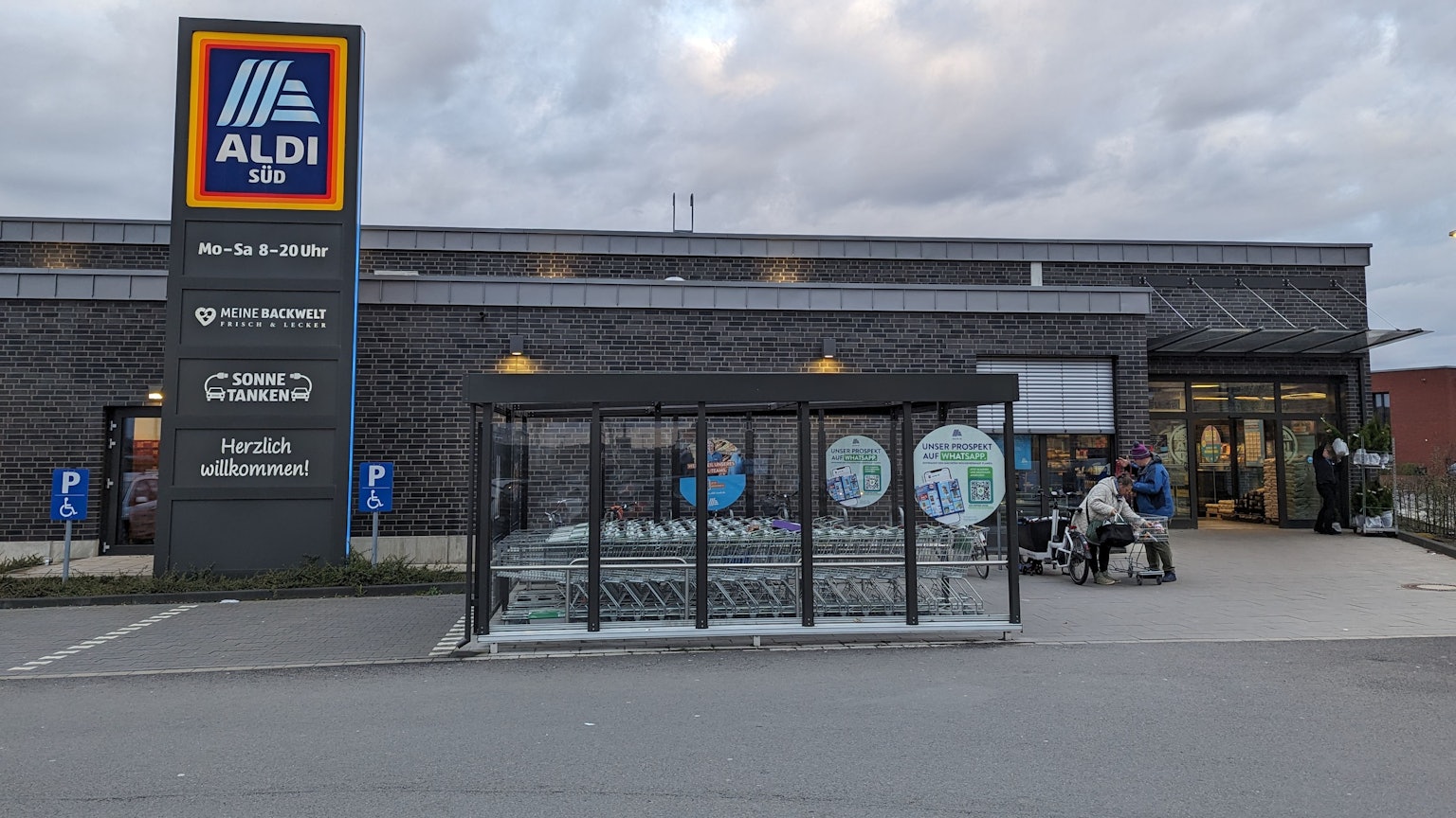 Ein Aldi-Markt mit Klinkerfassade, Unterstellplatz für Einkaufswagen und einer großen Stele mit Aldi-Schild.