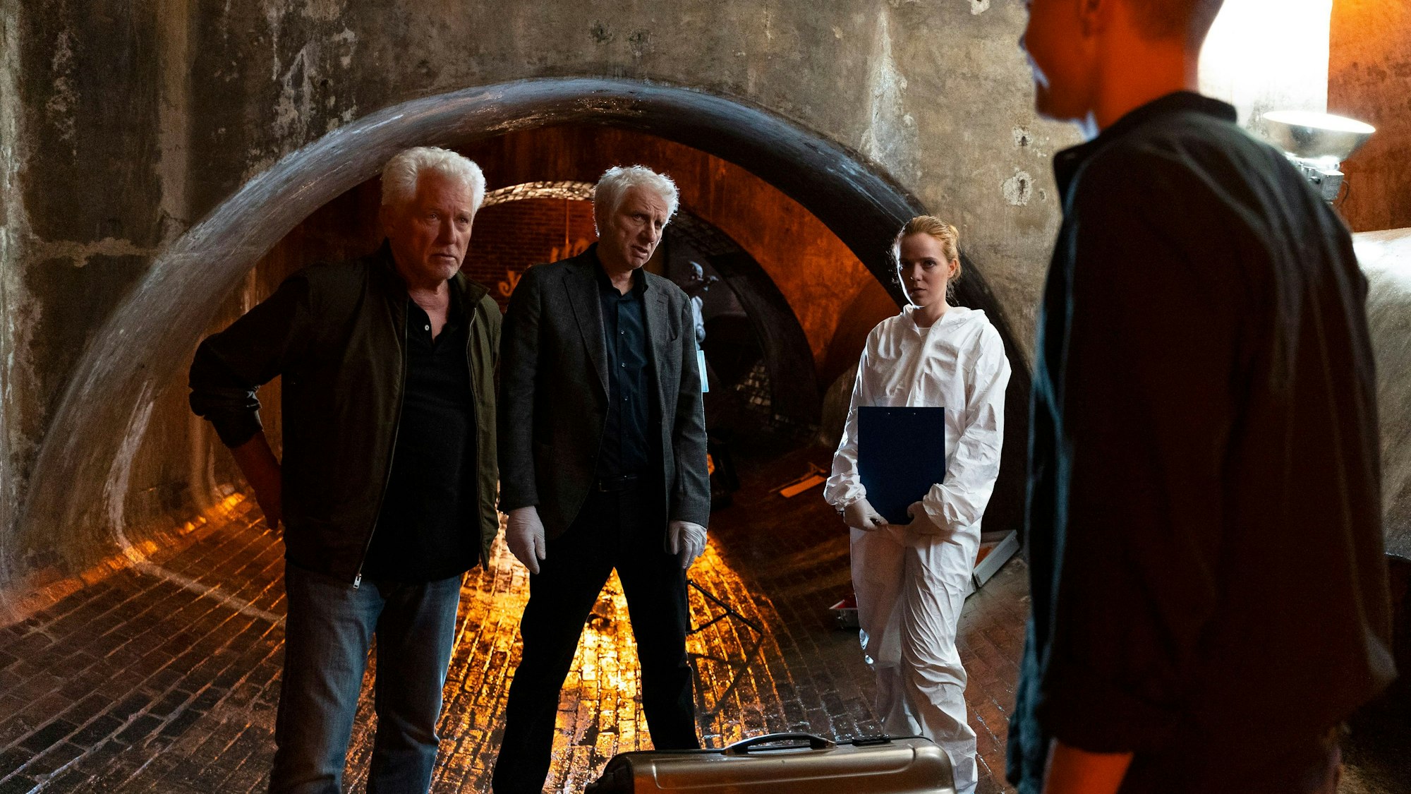 Auf dem Bild sind die Ermittler in einem Tunnel zu sehen. Kalli Hammermann ist im Vordergrund, die beiden älteren Ermittler und die Rechtsmedizinerin schauen ihn an.