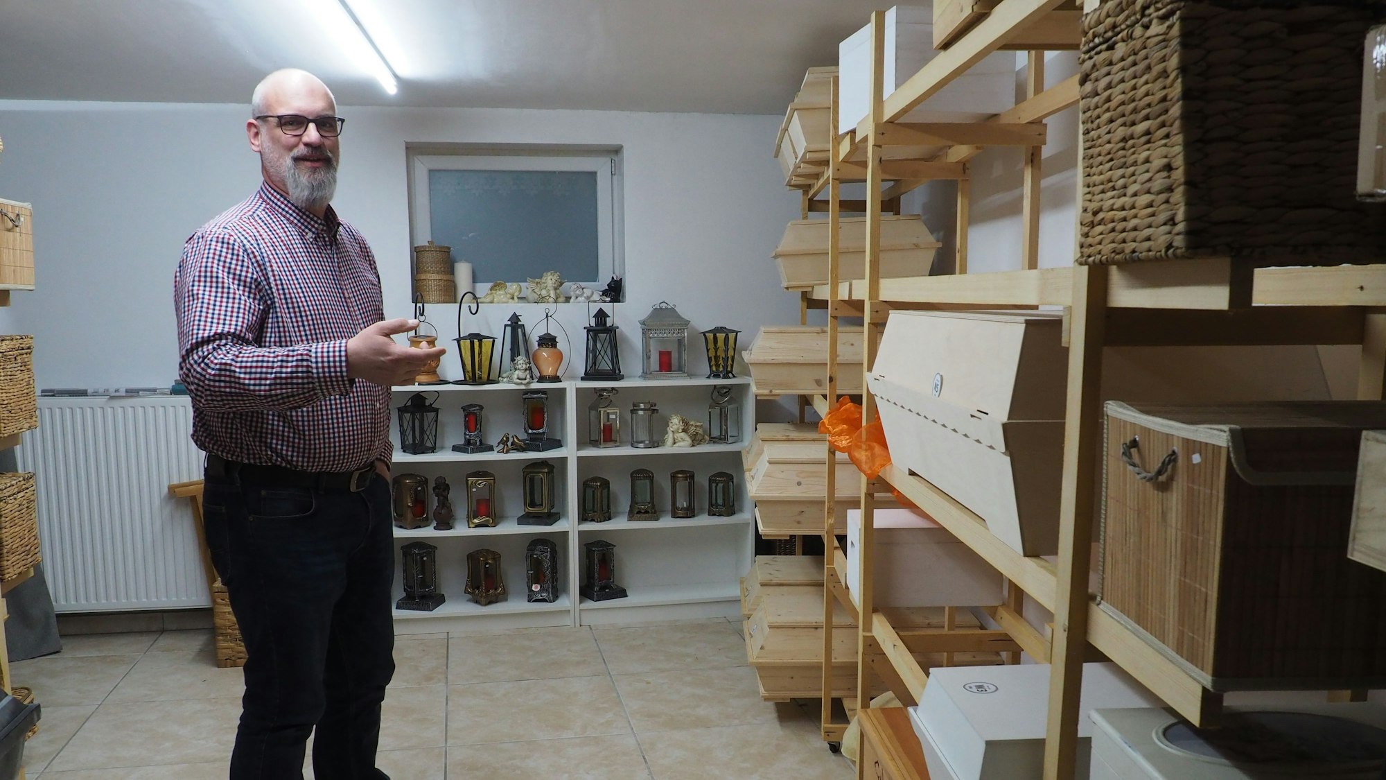 Zu sehen ist ein Mann vor einem Regal mit Särgen.