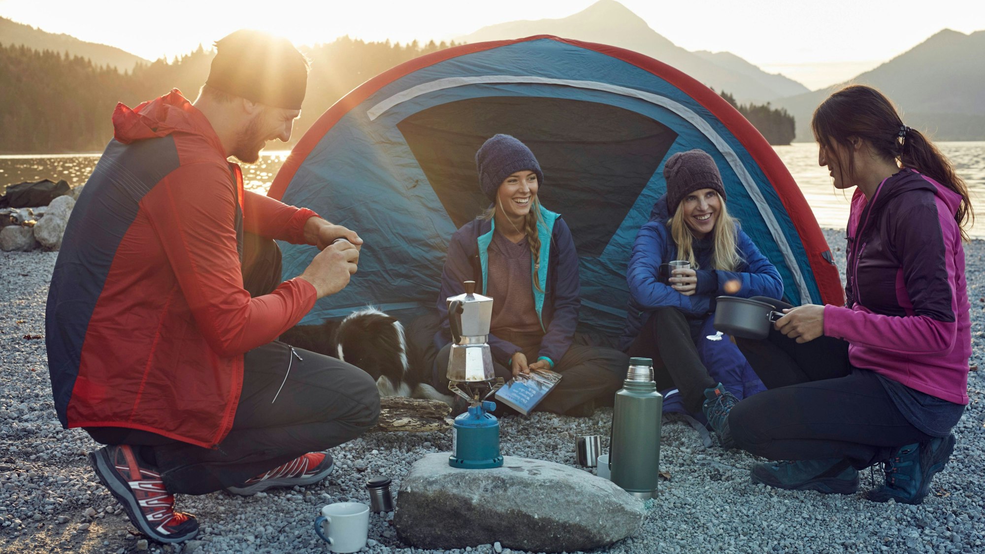 Eine Trekking-Gruppe kocht vor einem Zelt Kaffee auf einem Gaskocher.