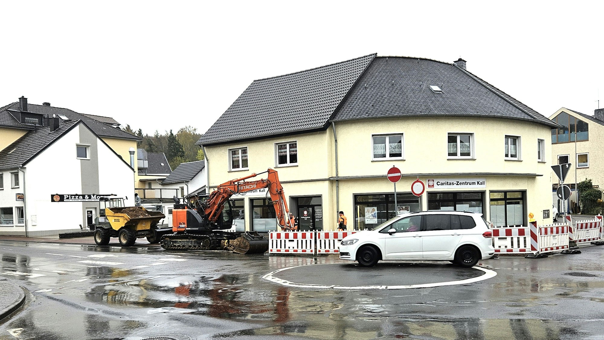 Ein Bagger ist am Kreisverkehr Aachener Straße/Bahnhofstraße im Einsatz. Ein weißes Auto fährt an der Baustelle vorbei.