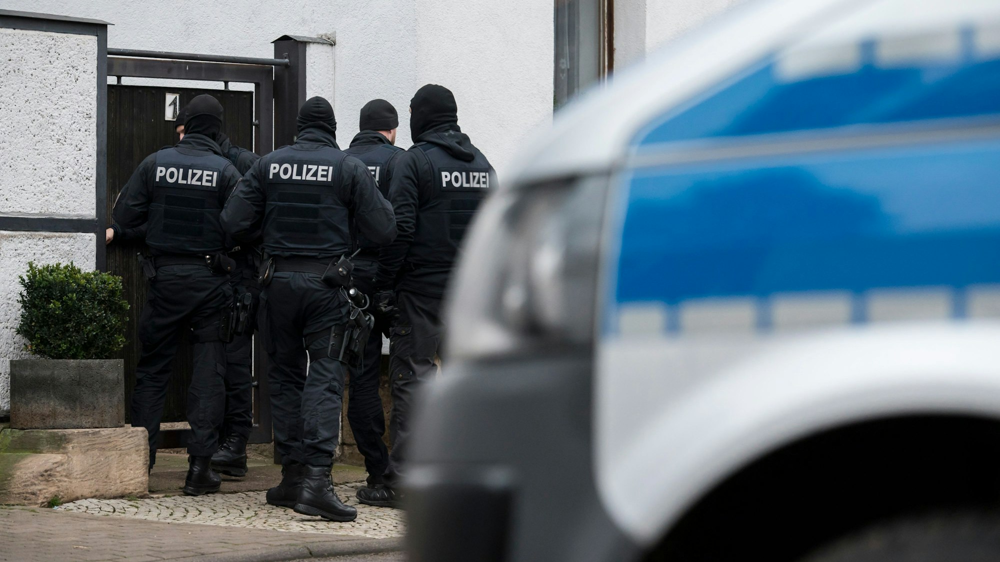Polizisten und ein Polizeiwagen stehen vor einem Wohnhaus.