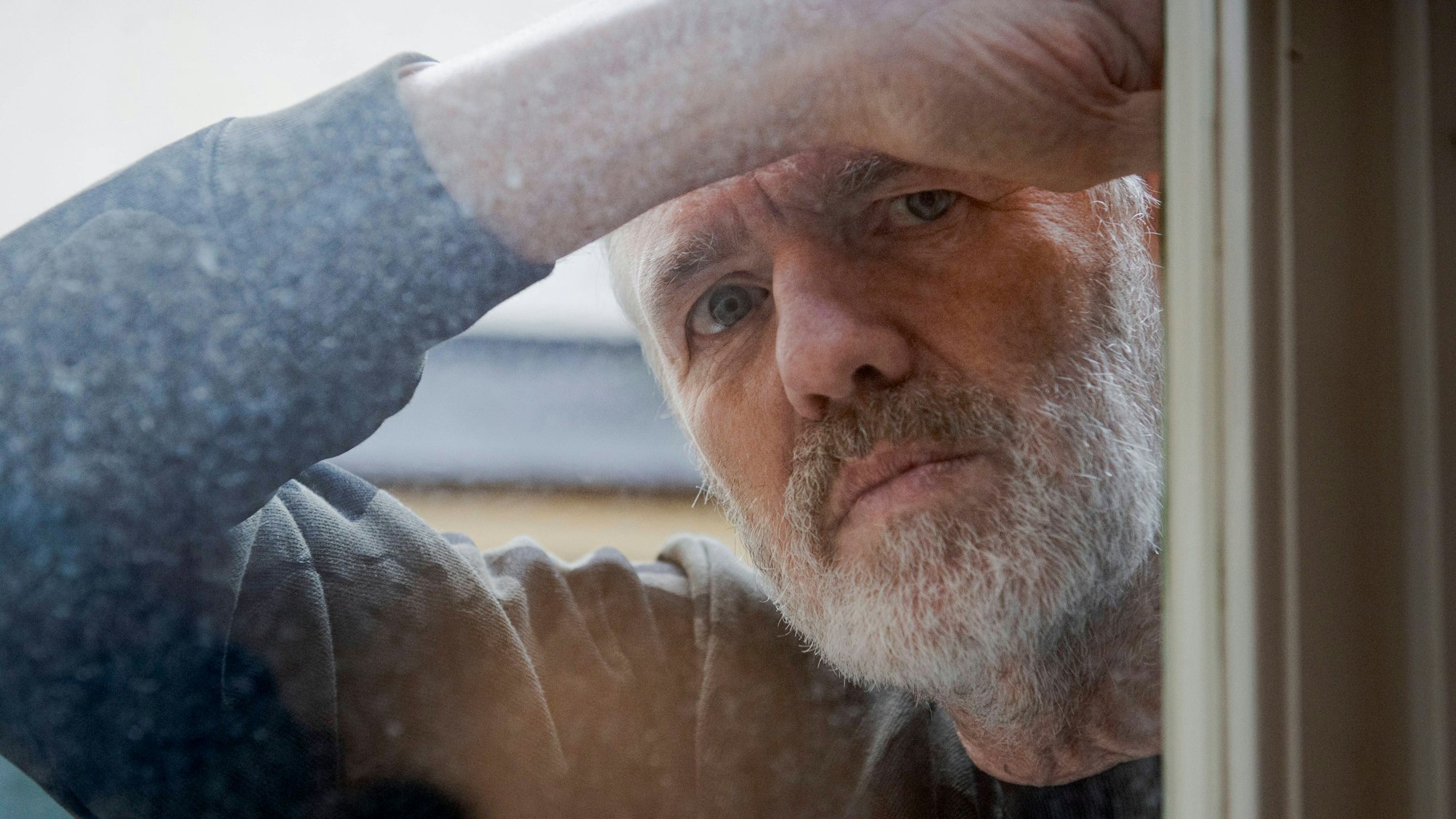 Der niederländische Fotograf Anton Corbijin blickt durch eine Fensterscheibe.