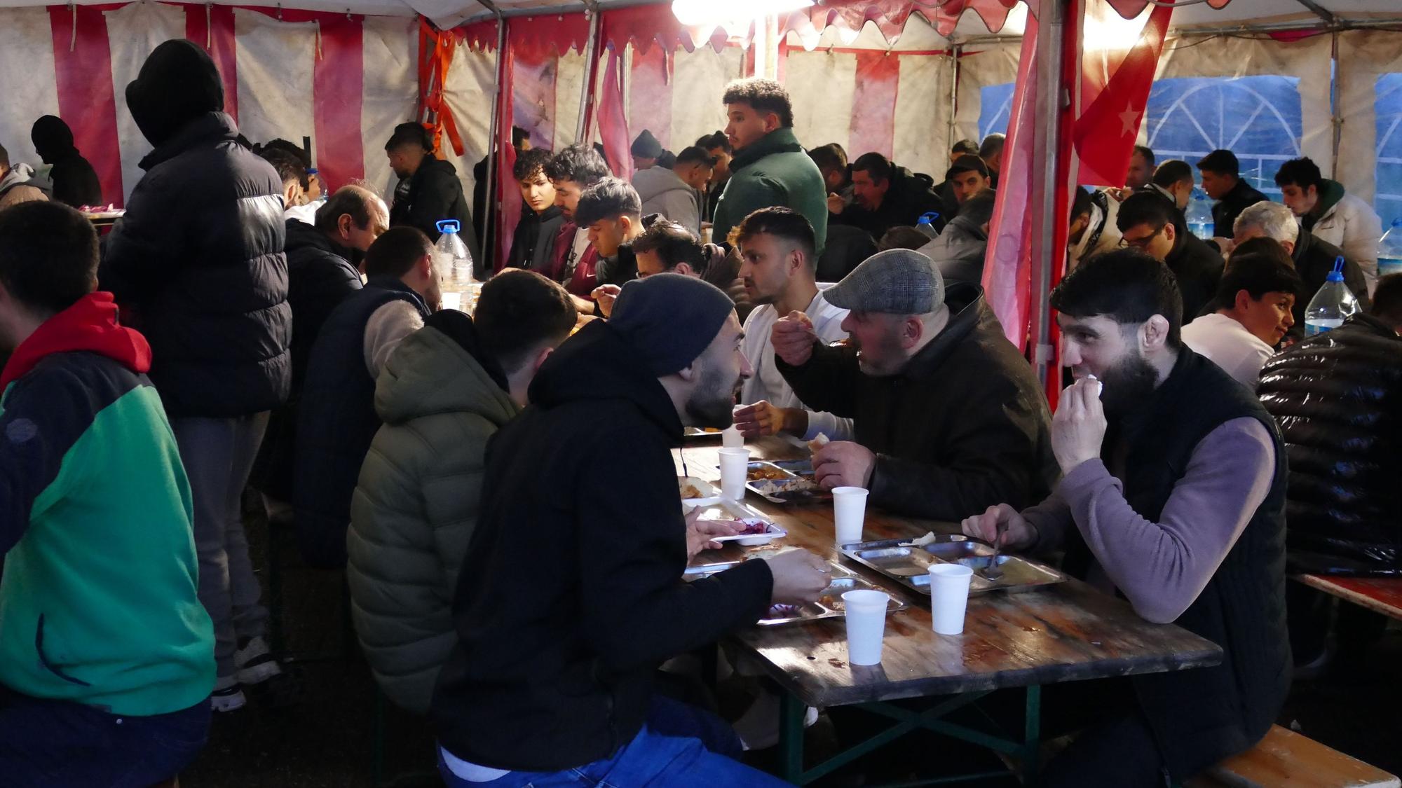 Männer sitzen an Biertischen in einem Zelt, sie essen.