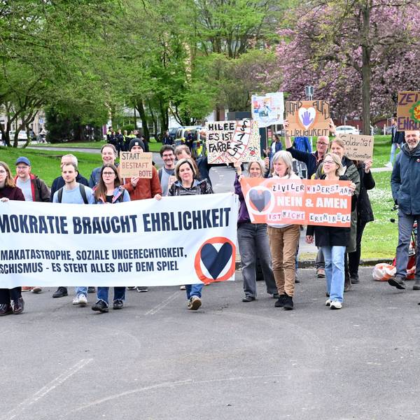 Unterstützer der „Letzten Generation“ laufen eine Straße entlang und halten Plakate hoch.