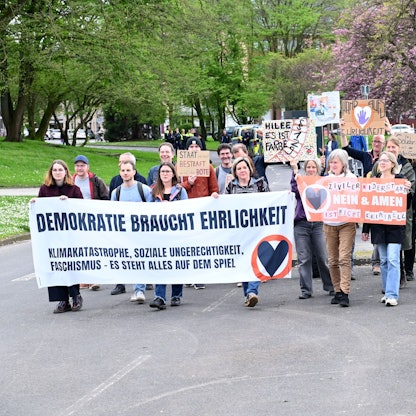 Unterstützer der „Letzten Generation“ laufen eine Straße entlang und halten Plakate hoch.
