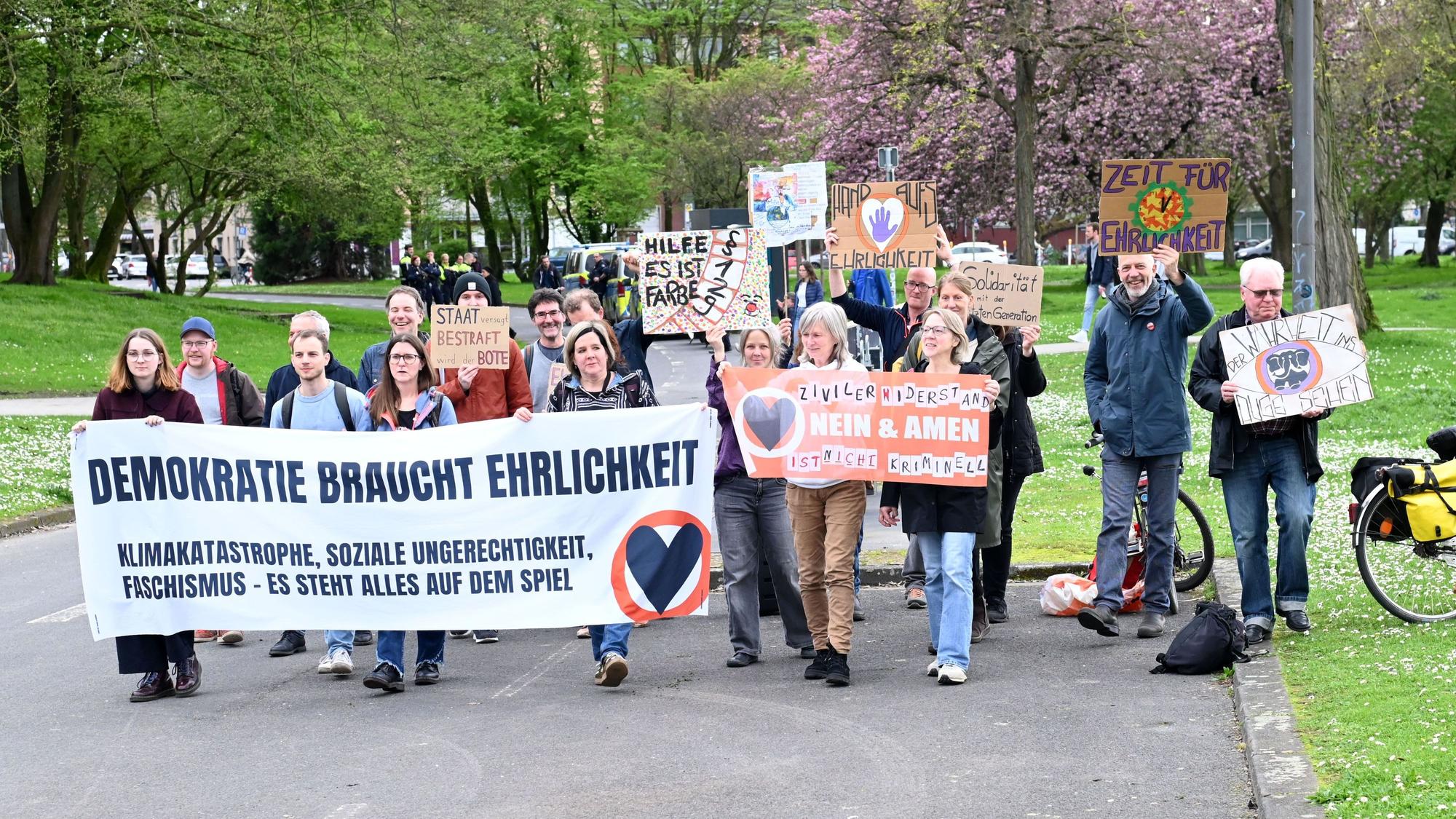 Unterstützer der „Letzten Generation“ laufen eine Straße entlang und halten Plakate hoch.