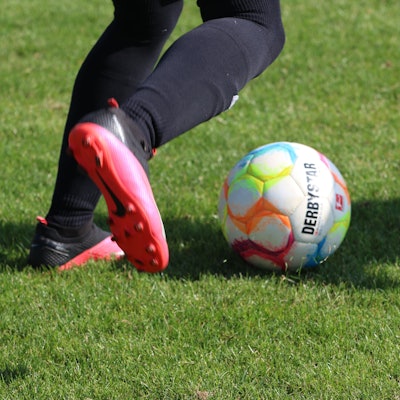Die Füße eines Fußballspielers in pink-schwarzen Schuhen sind zu sehen, kurz bevor er einen Ball schießt.