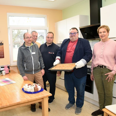 Eine Gruppe steht in einer Küche und hantiert mit Kuchen.