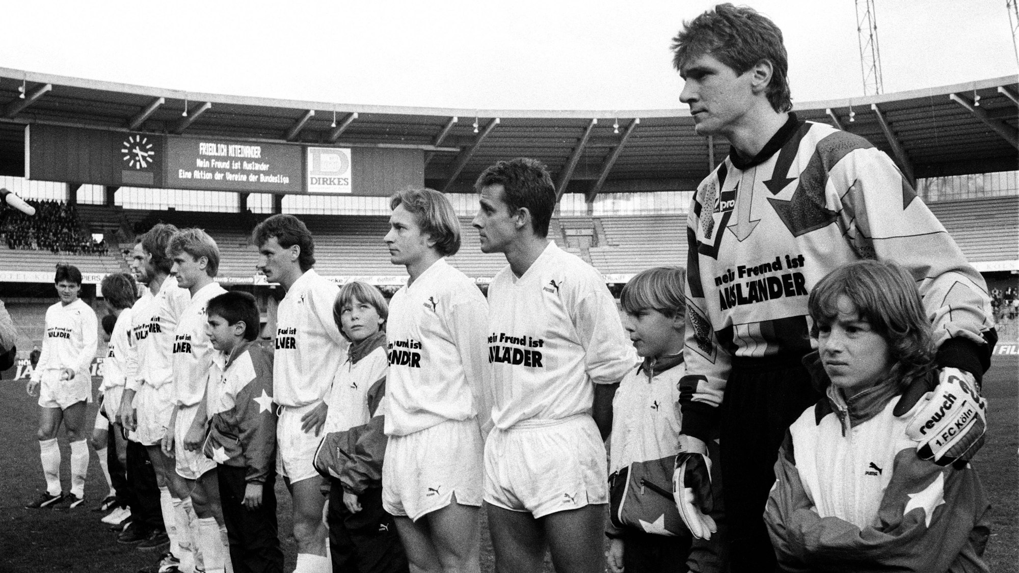 Auf der Schwarz-Weiß-Fotografie steht die Mannschaft des 1. FC Köln auf dem Rasen vor fast leeren Zuschauerrängen im Müngersdorfer Stadion.