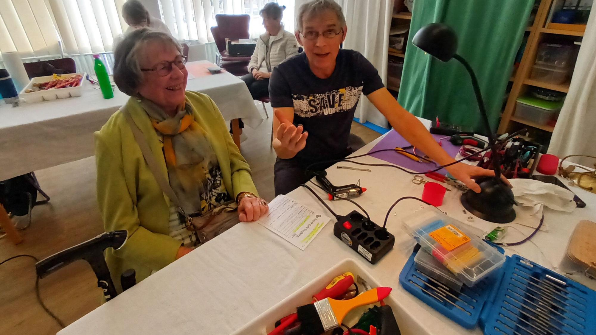 Eine Mann und eine Frau an einem Tisch, darauf Werkzeuge und eine Lampe