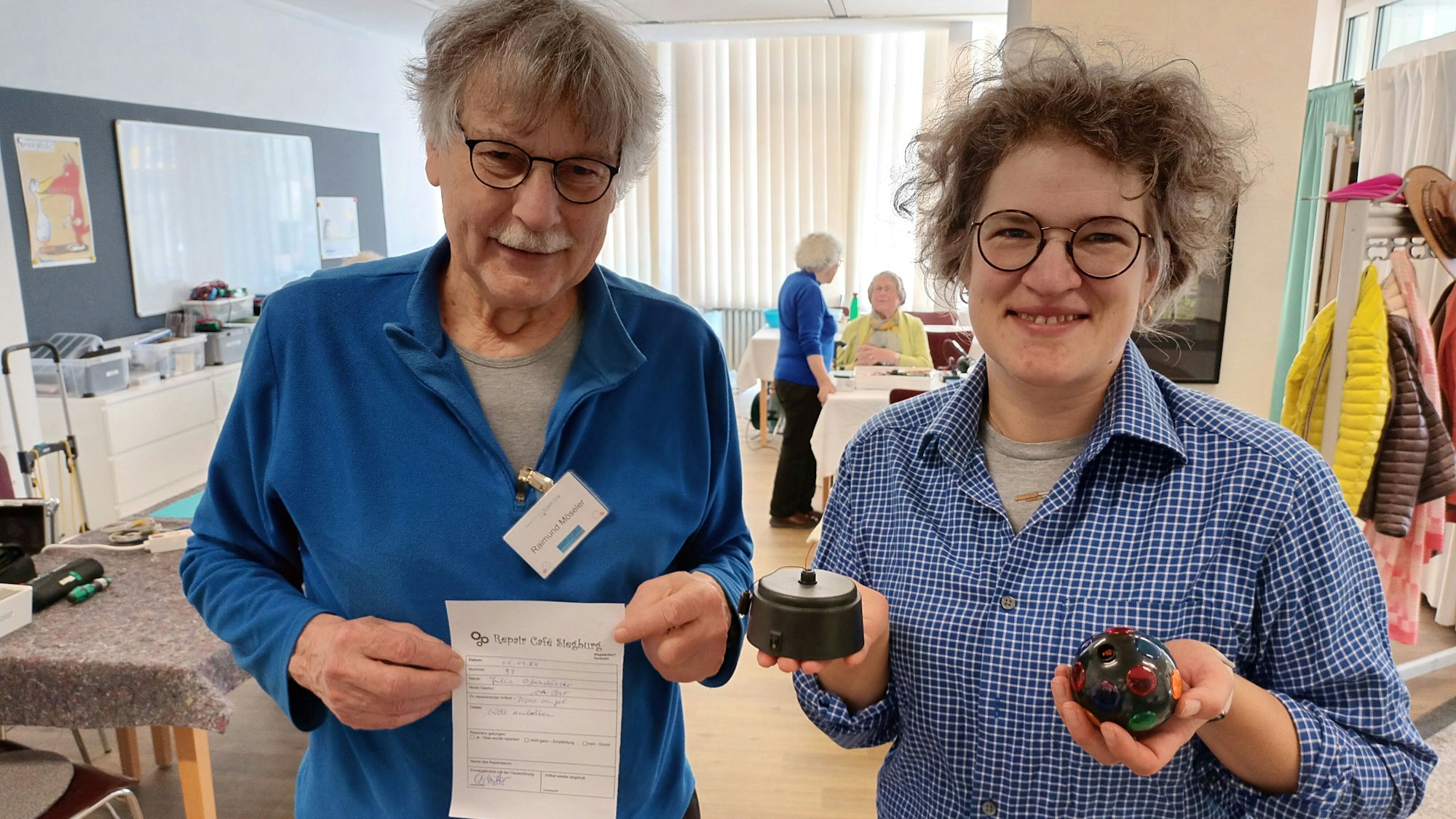 Eine Frau mit Brille hält eine kleine Disco-Kugel in der Hand, ein Mann mit Schnauzbart neben ihr zeigt ein Zertifikat.