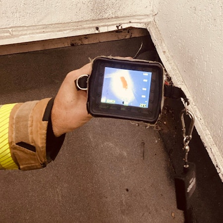 Ein Feuerwehrmann hält eine Wärmekamera auf den Abschluss eines frisch mit Dachpappe verschweißten Daches, unter dem offenbar ein Schwelbrand ausgebrochen ist.