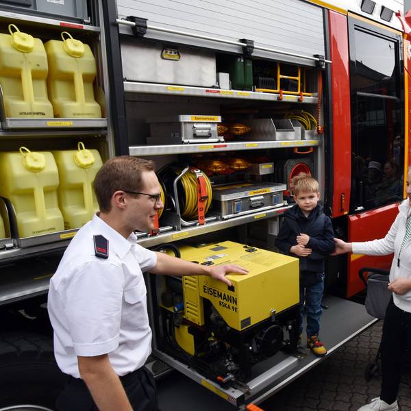 Ein Feuerwehrmann erläutert einer jungen Familie die Ladung eines Feuerwehrautos.