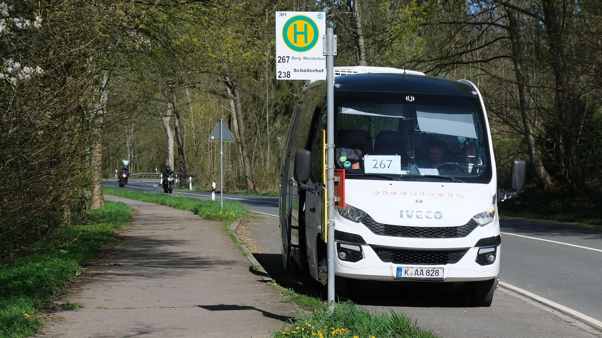 Zu sehen ist ein Bus an einer Bushaltestelle am Straßenrand.