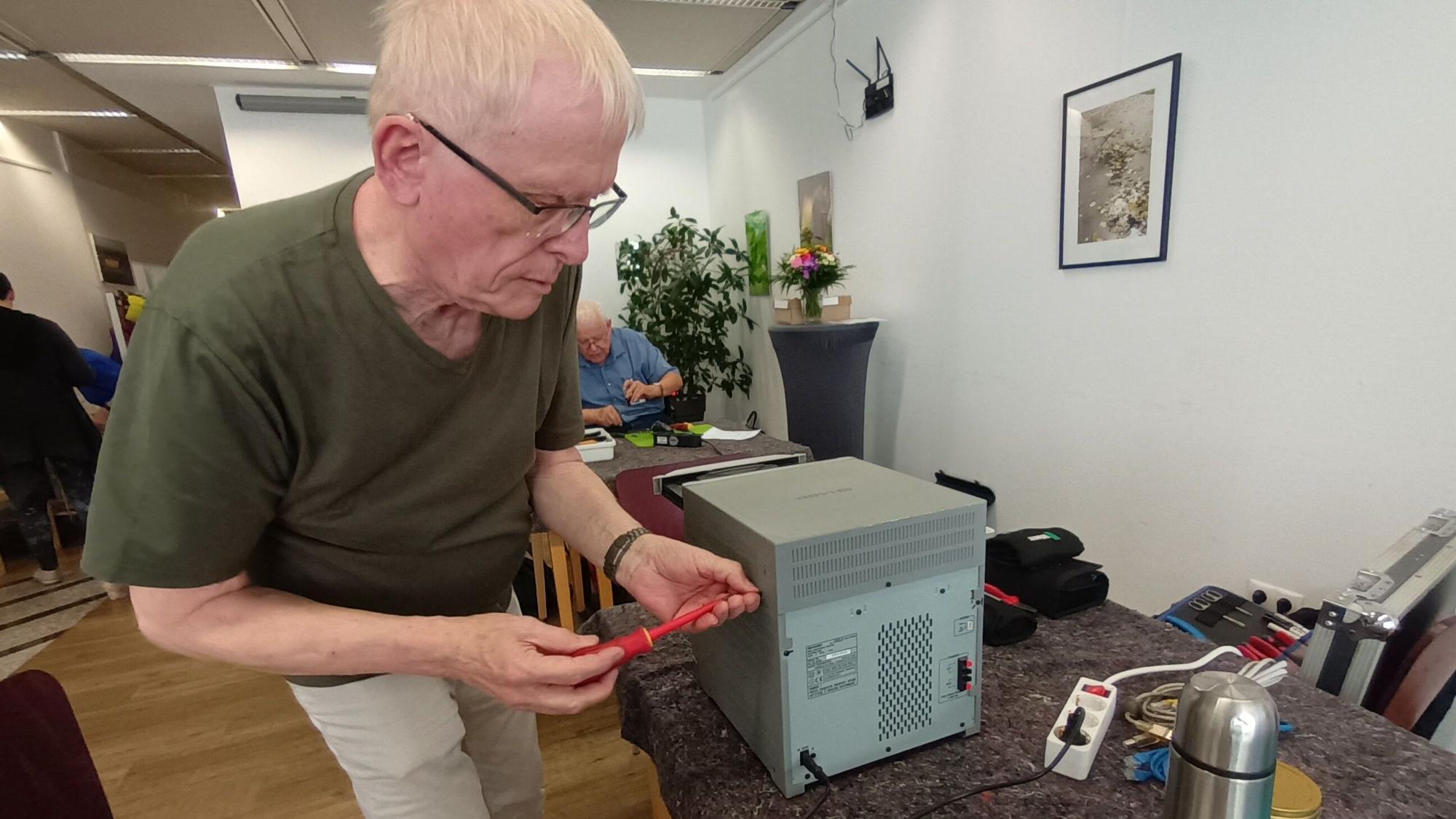 Ein Mann mit Brille schraubt an einem CD-Player.