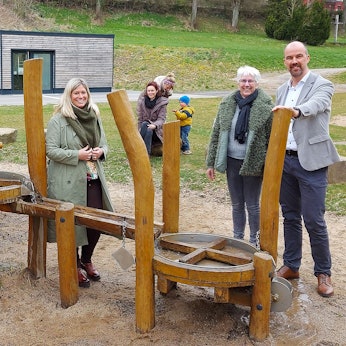 Bürgermeisterin Jennifer Meuren, Annegret Dreimüller und Guido Waters stehen am Kleinkinderspielplatz. Einige Kinder spielen.
