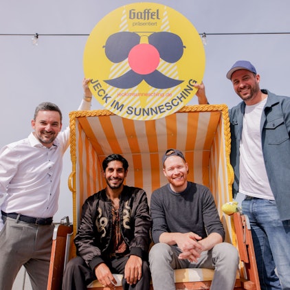 Björn Lindert, geschäftsführender Gesellschafter x4kids, Juri Rother (Planschemalöör), Nils Schreiber (Miljö) und Martin Becker, Geschäftsführer Sharkys Schwimmschule sitzen am Rhein in einem Strandkorb.