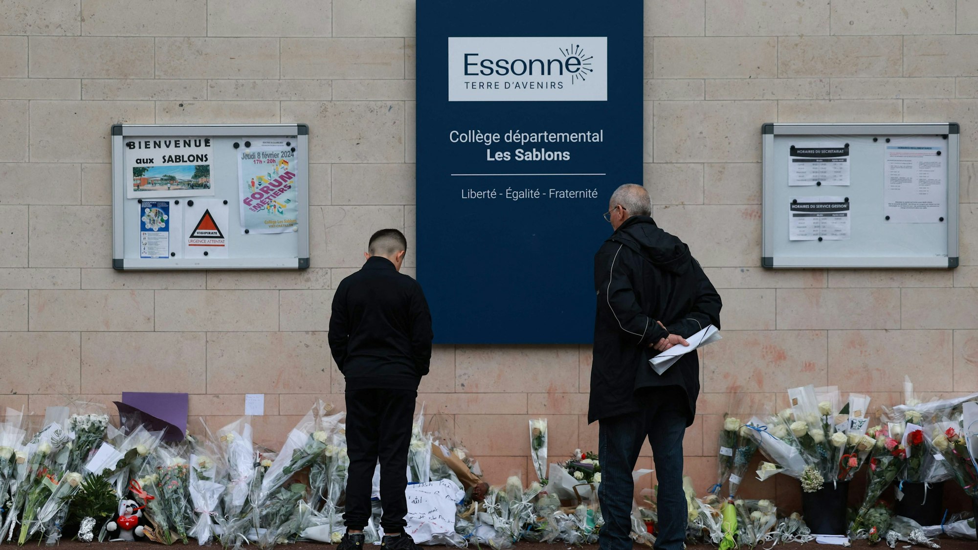 Anwohner betrachten die Blumen, die vor dem Eingang der Mittelschule Les Sablons in Viry-Chatillon niedergelegt worden sind.