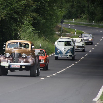 Fünf Oldtimer fahren hintereinander auf einer Straße.