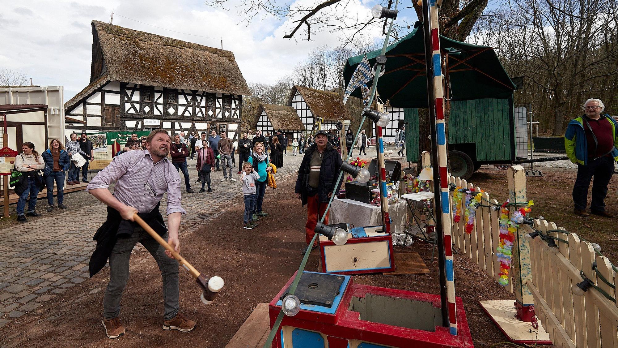 Ein Besucher des historischen Jahrmarkts schwingt den Hammer beim „Hau den Lukas“. Im Hintergrund stehen Fachwerkhäuser.