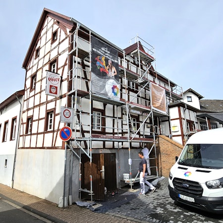 Blick auf das eingerüstete Gasthaus Gier. Mitarbeiter einer Malerfirma sind bei der Arbeit.