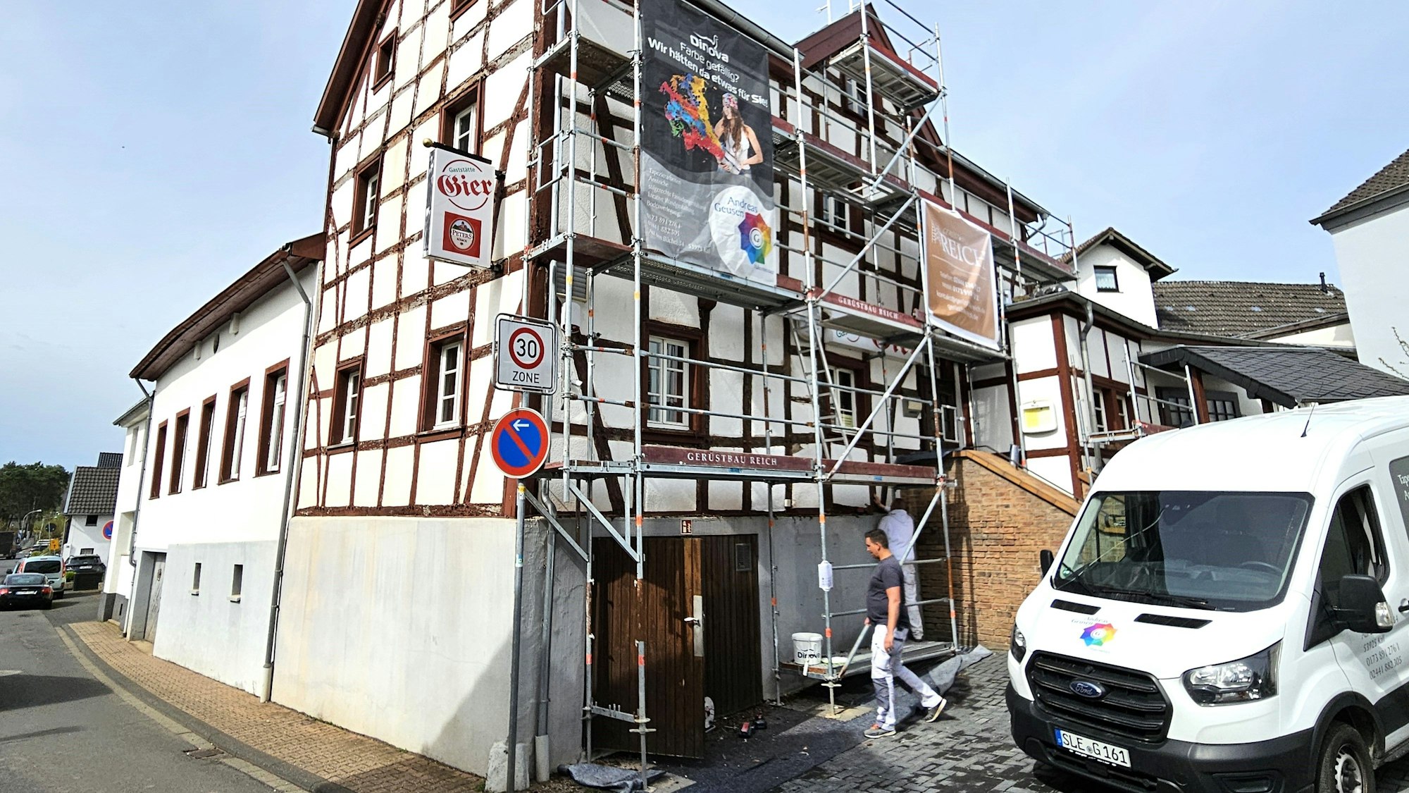 Blick auf das eingerüstete Gasthaus Gier. Mitarbeiter einer Malerfirma sind bei der Arbeit.